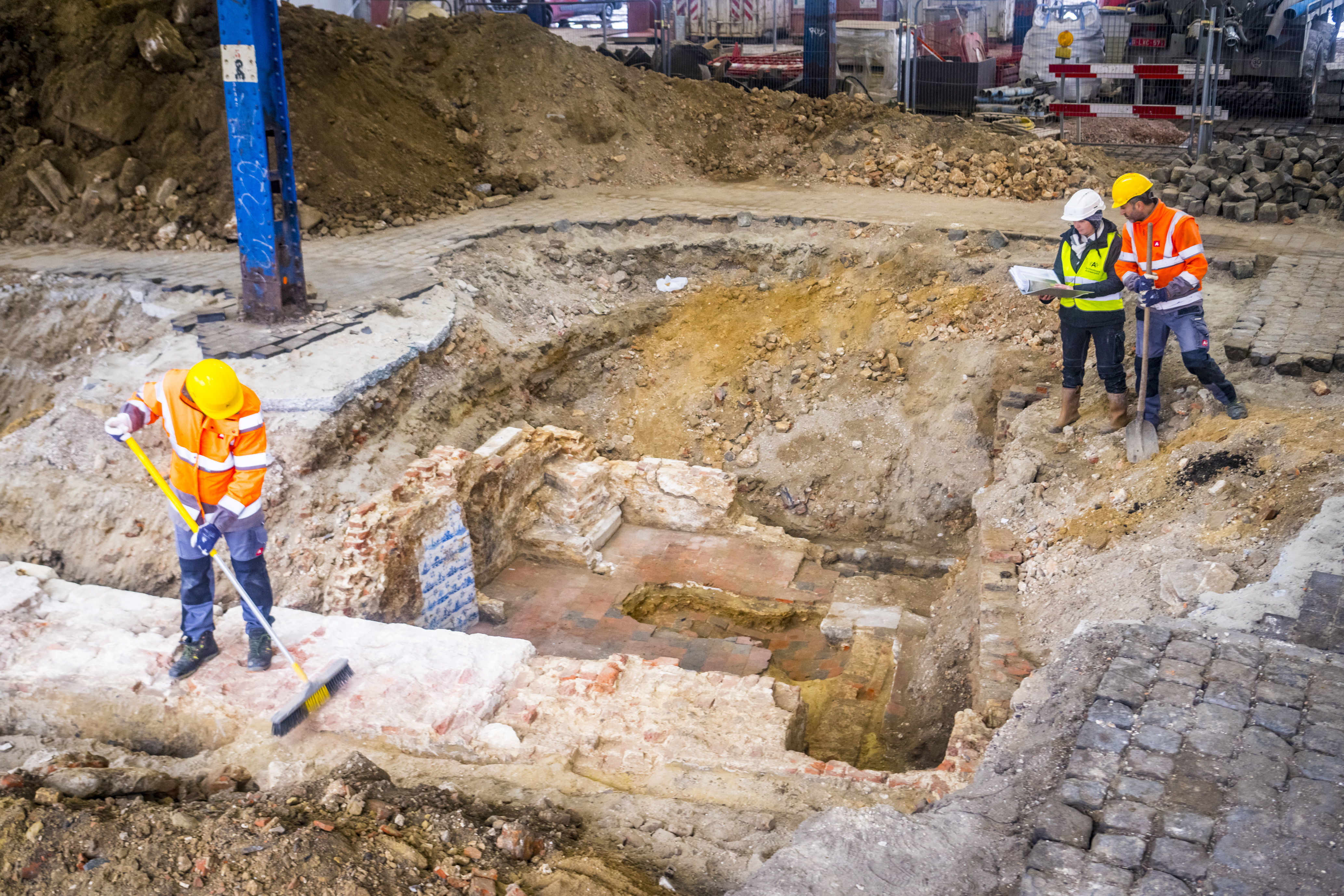 Overzicht van de stadsmuur aan de Kleine Bierpoort met daarachter het havenhuis. In de hoek zijn blauwe Delftse tegels van de haard te zien. De archeologen zijn aan het werk.