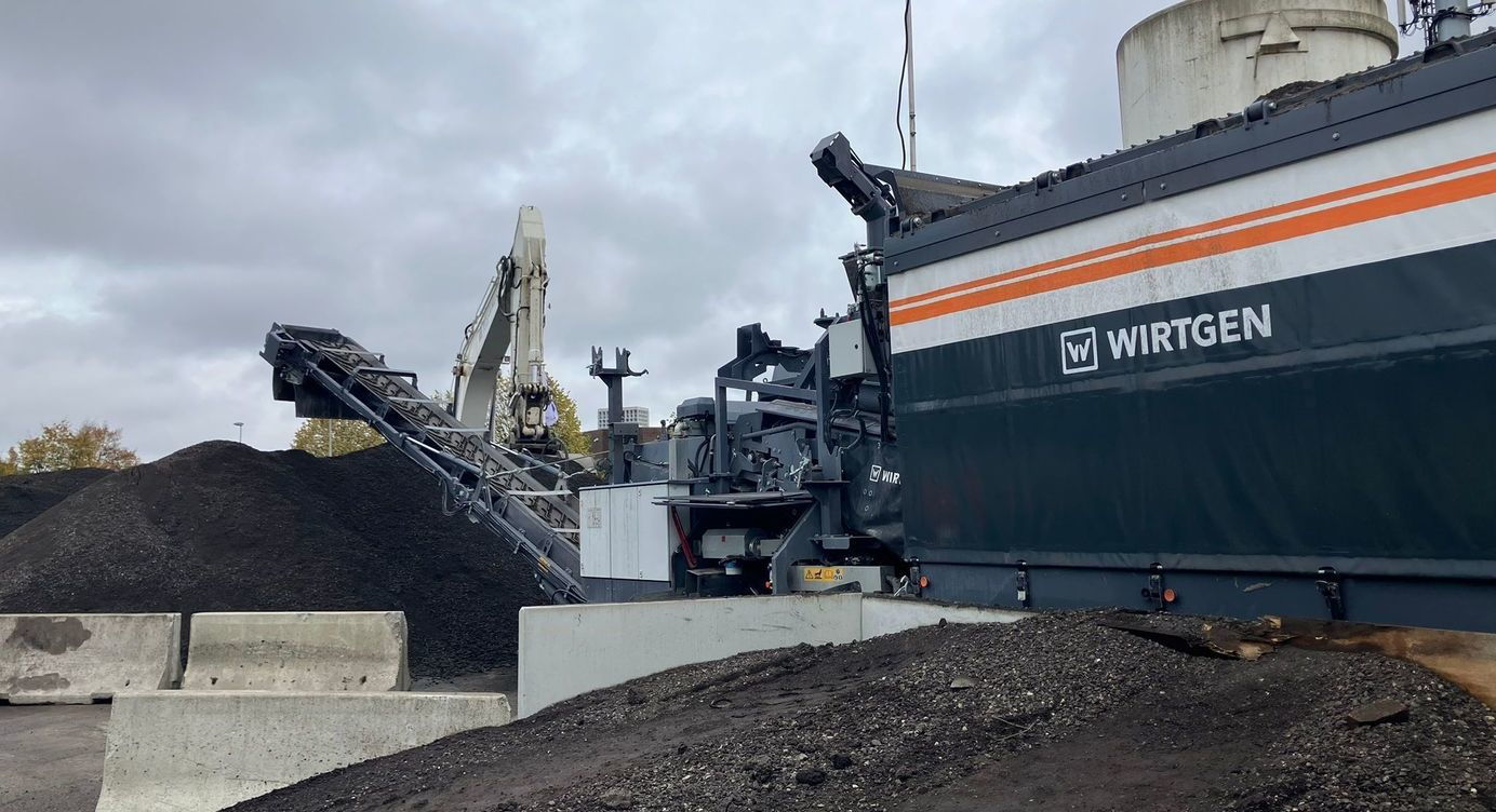 De asfaltverwerkingsmachine mengt het gebroken asfalt met een klein beetje cement, water en een specifiek bindmiddel, genaamd schuimbitumen. Na een minuut mengen op omgevingstemperatuur komt de fundering er langs de andere zijde uit.