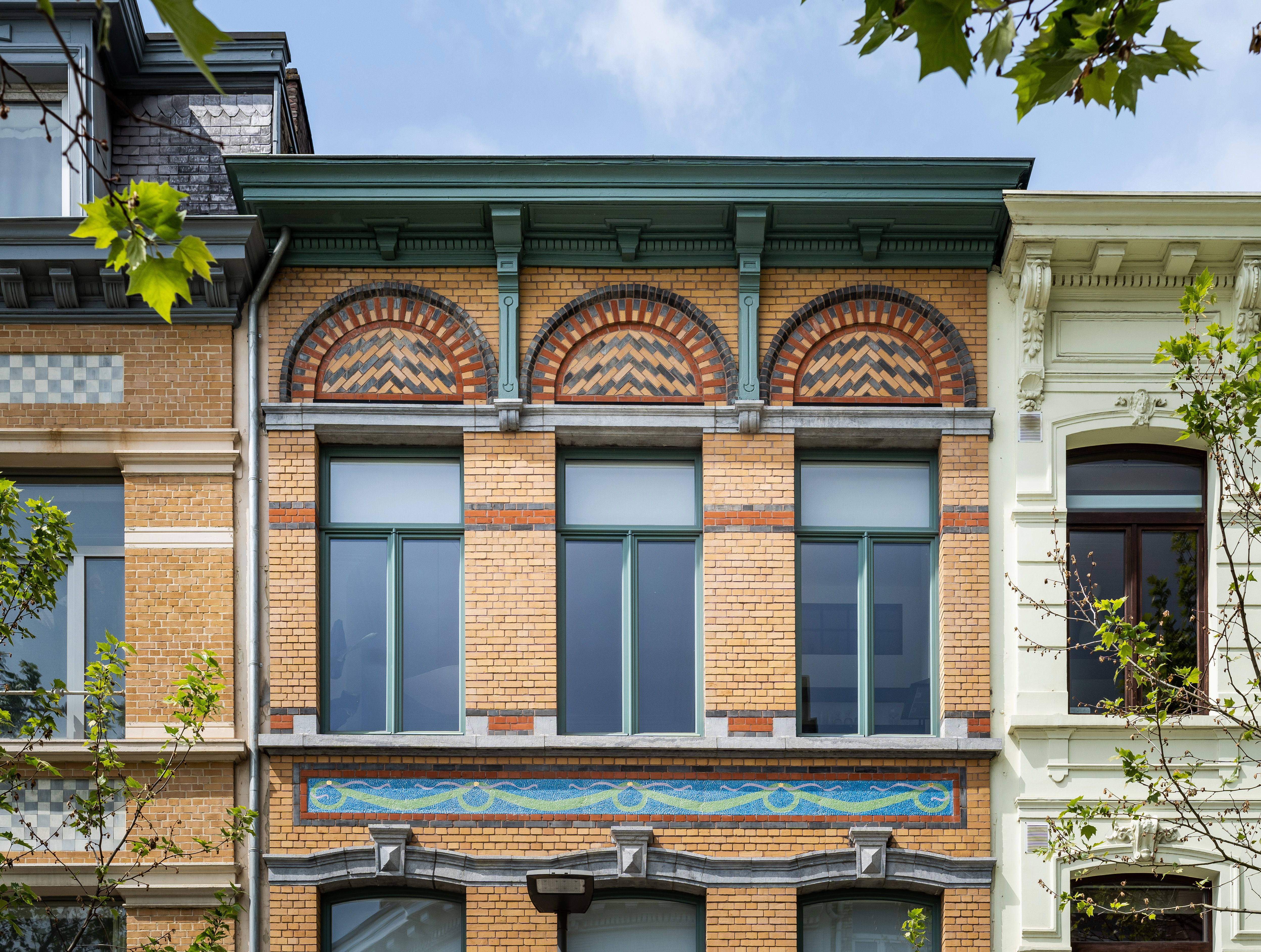 Gevel na de restauratie met gele bakstenen en kleurrijk mozaïek.
