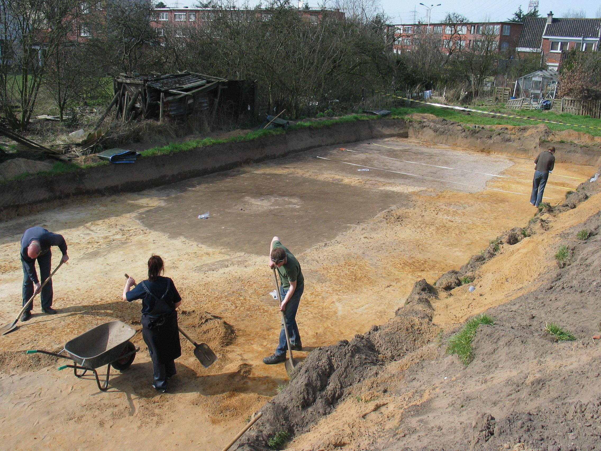 Opschave van het opgravingsoppervlak. Laag per laag wordt er grond verwijderd. Mogelijk verschijnen er dan archeologische sporen of objecten.