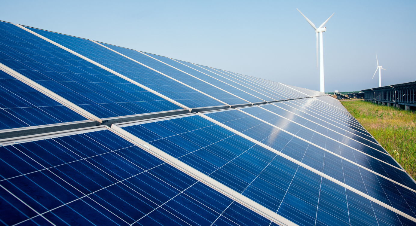 Zonnepanelen op een grasveld en windmolens op de achtergrond