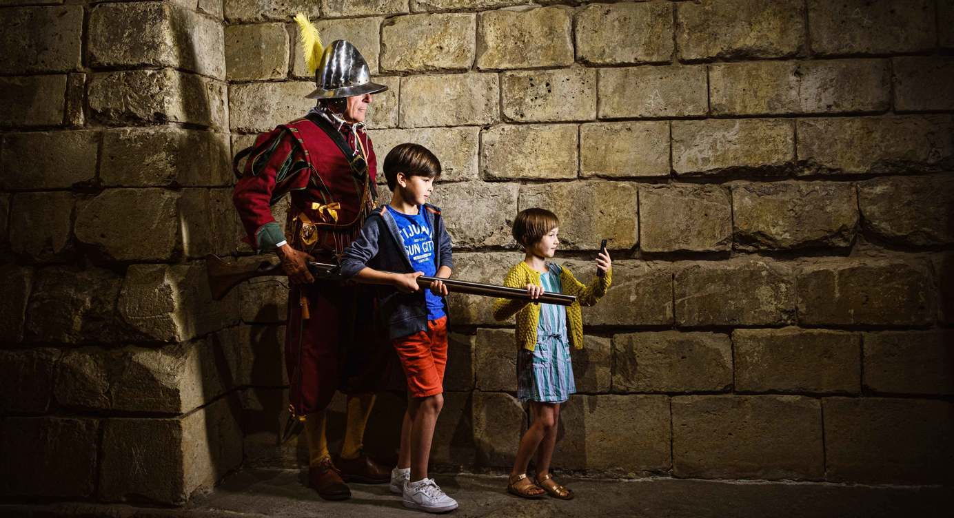 Twee kinderen zijn op stap met de Spaanse soldaat langs tal van archeologische locaties in Antwerpen. 
De Antwerp Museum App toont de weg.