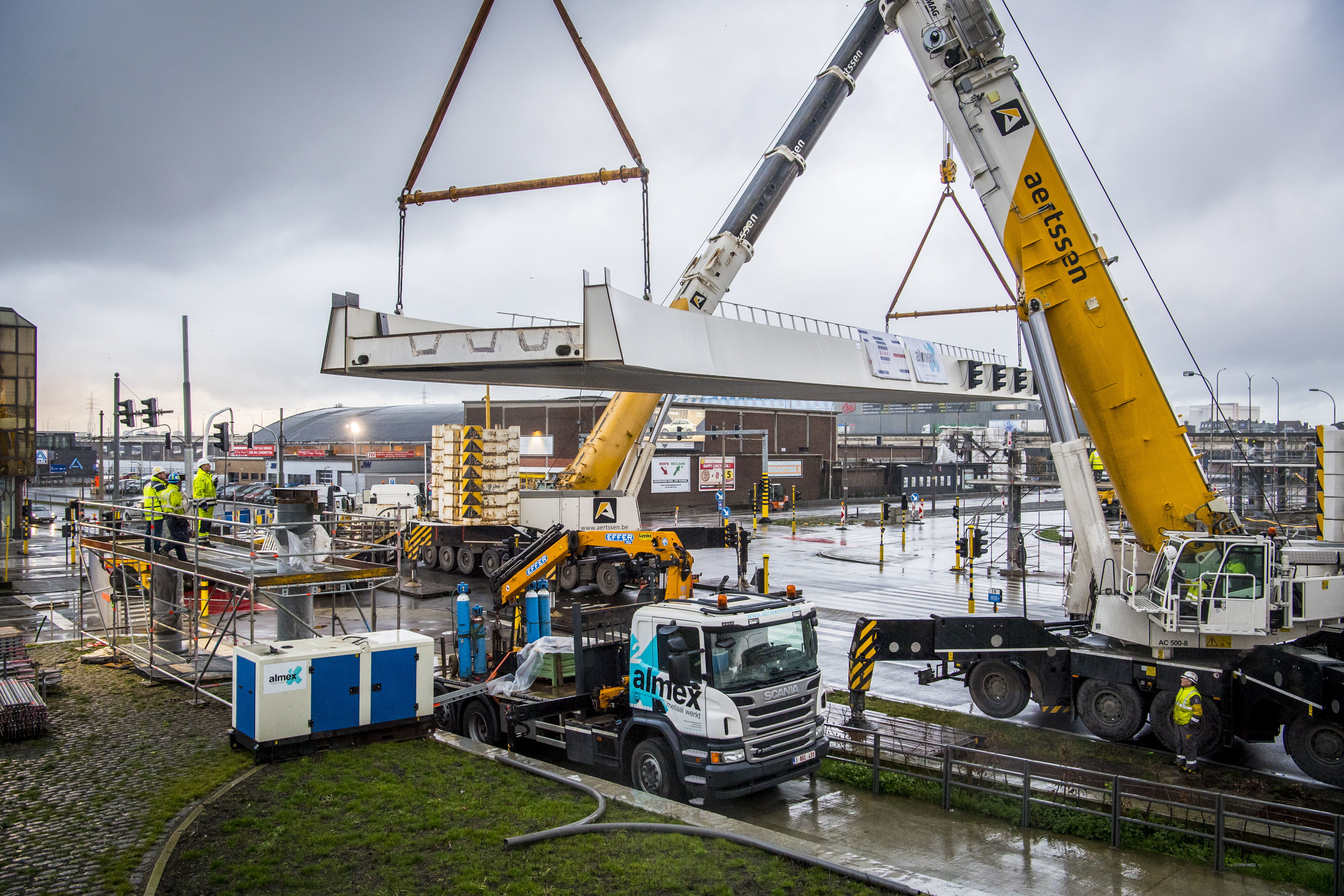 De twee kranen hijsen het eerste brugdeel op zijn plaats.